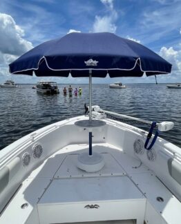 View from the bow of a white boat with a dark blue canopy, calm water, and distant boats on the horizon.