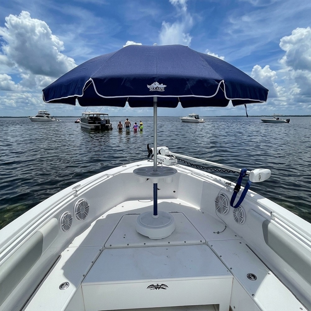 View from the bow of a white boat with a dark blue canopy, calm water, and distant boats on the horizon.