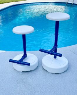Two white round-seated pool stools with blue poles on a concrete pool deck beside a blue swimming pool.