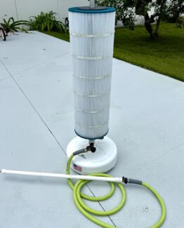 Portable pool filter with a tall pleated cartridge on a white base, resting on a gray concrete patio with a coiled lime-green hose nearby.