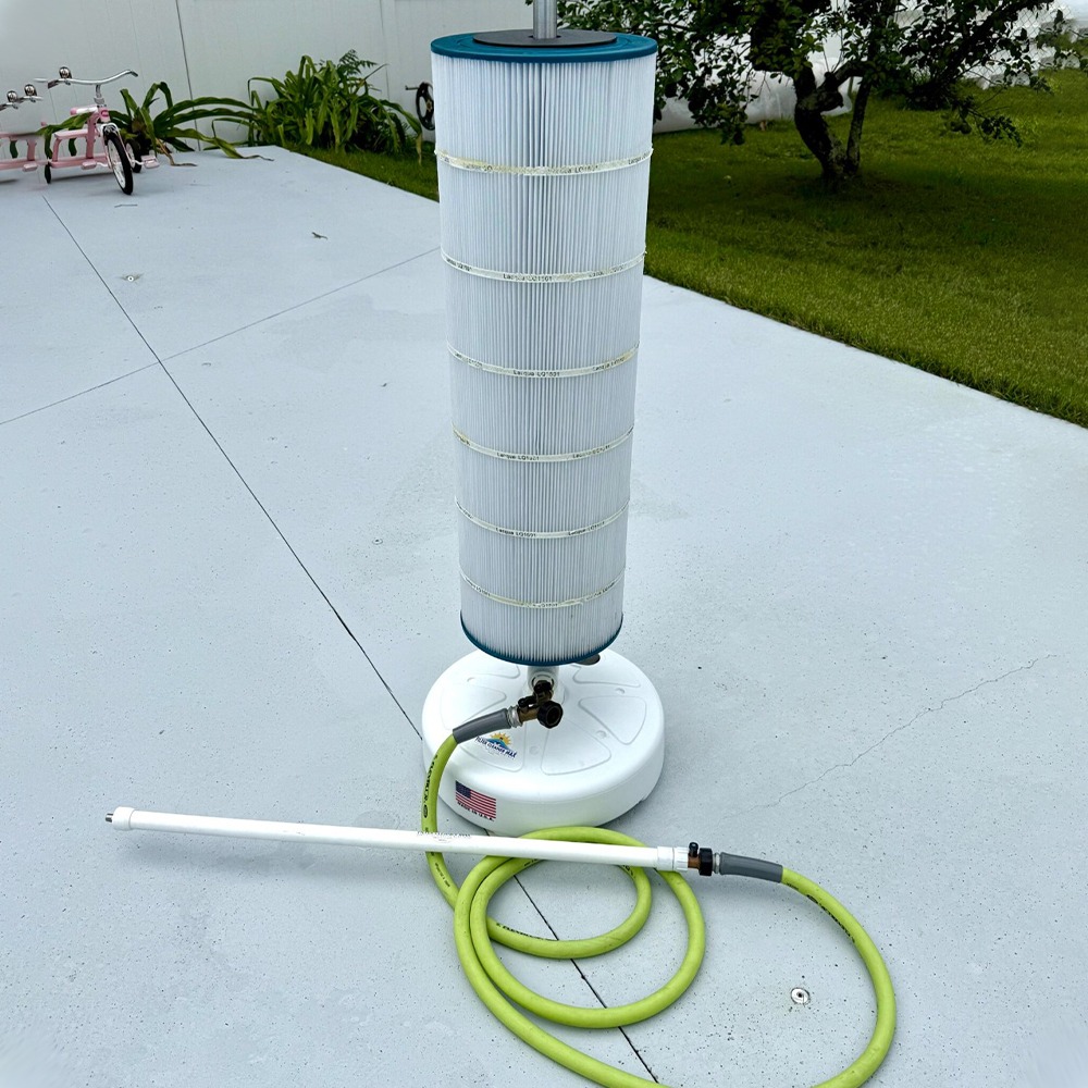 Portable pool filter with a tall pleated cartridge on a white base, resting on a gray concrete patio with a coiled lime-green hose nearby.