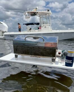 Portable stainless steel grill mounted on a white floating platform on open water, with boats and people in the background.