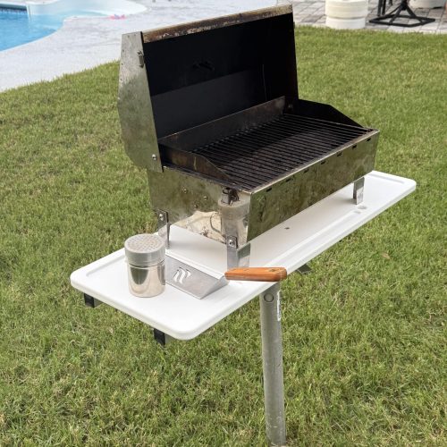 Photo of a grill on a portable grill and schill table top in the grass.
